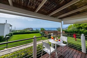 A balcony with a table and chairs, overlooking a green lawn and a view of the sea. - Sea View - 40 Parallelo - Superior+ 18, Marina di Camerota, Italy (Marina di Camerota)