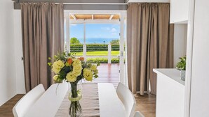 A dining area with a table, chairs, and a vase of flowers. There is a view of a green landscape and the sea through a glass door. - Sea View - 40 Parallelo - Superior+ 17, Marina di Camerota, Italy (Marina di Camerota)