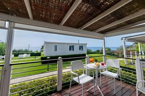 A covered outdoor area with white chairs and a table, overlooking a white house and the sea. - Sea View - 40 Parallelo - Superior+ 17, Marina di Camerota, Italy (Marina di Camerota)