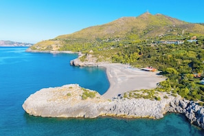 Eine Küstenlandschaft mit blauem Meer, felsiger Küste und einem Hügel mit verstreuten Gebäuden.