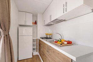 Eine kleine Küche mit weißen Schränken, einem eingebauten Ofen, einem Gasherd und einem Spülbecken.