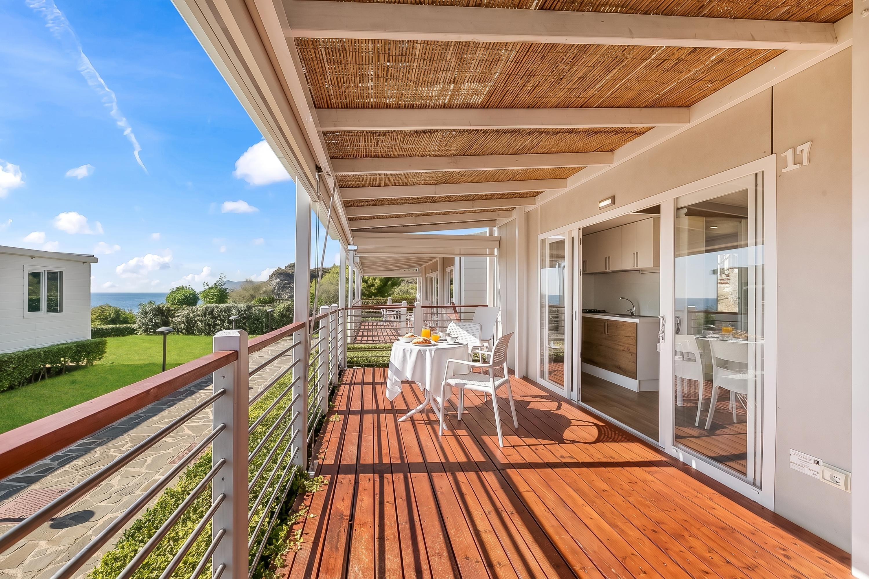 Een balkon met een houten terras, witte meubels en uitzicht op zee.