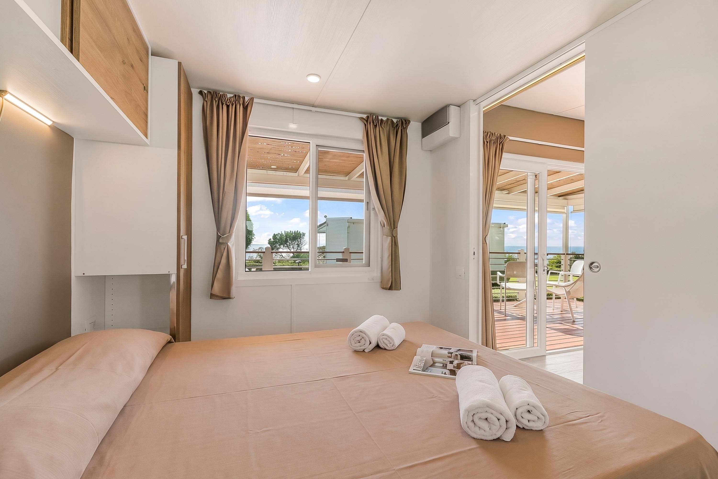 Habitación de hotel con cama, ventana con cortinas, vistas al exterior y puerta que da a un balcón.