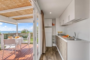 A compact kitchen with a view of the sea, a dining area with a table and chairs, and a wooden deck. - Sea View - 40 Parallelo - Superior+ 16, Marina di Camerota, Italy (Marina di Camerota)
