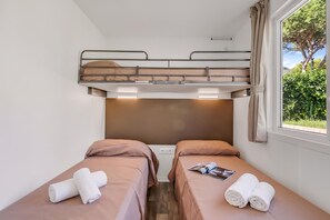 Ein kleines, gemütliches Zimmer mit zwei Einzelbetten, einem Schlafplatz oben in Etagenform und einem Fenster mit Blick auf Grünflächen.