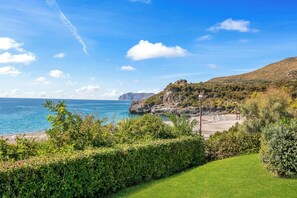 Un paysage côtier comprenant une zone herbeuse, une falaise rocheuse et un ciel bleu dégagé.