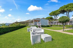Une villa moderne dotée d’un espace extérieur aménagé avec un coin salon couvert, d’une pelouse bien entretenue et d’une vue sur le paysage environnant.