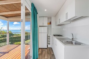 Une cuisine compacte avec vue sur l’océan, un balcon doté d’un plancher en bois et un rideau de couleur turquoise.