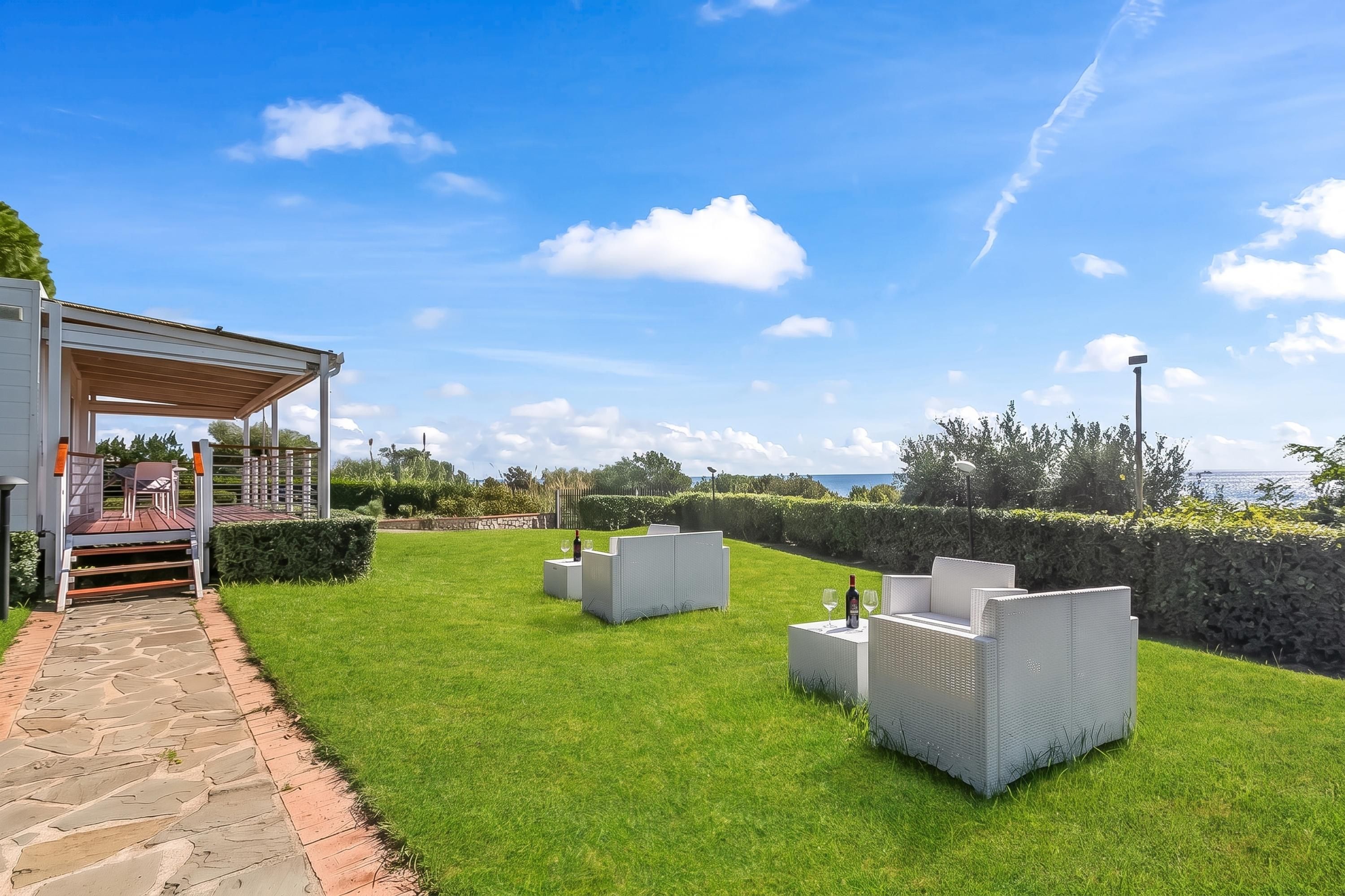 Un espace extérieur aménagé avec soin, comprenant une terrasse, une pergola, des sièges et une vue sur la mer.