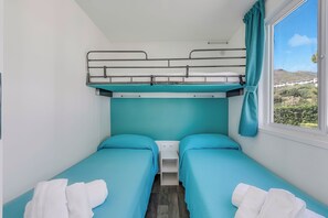 Une petite pièce compacte avec des lits superposés et un lit simple, une fenêtre donnant sur un paysage et une table de chevet blanche.