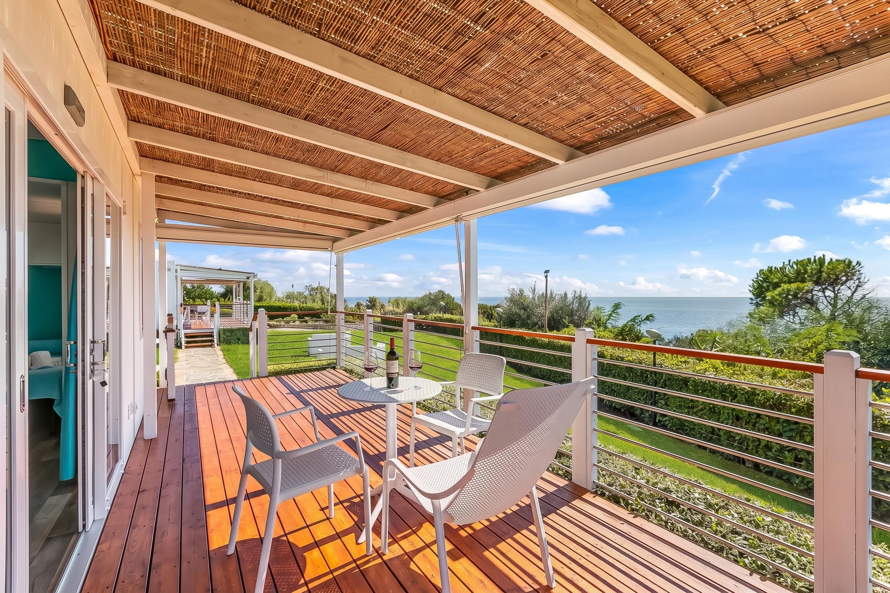 Una terraza techada al aire libre con piso de madera, sillas de metal blanco y una mesa.