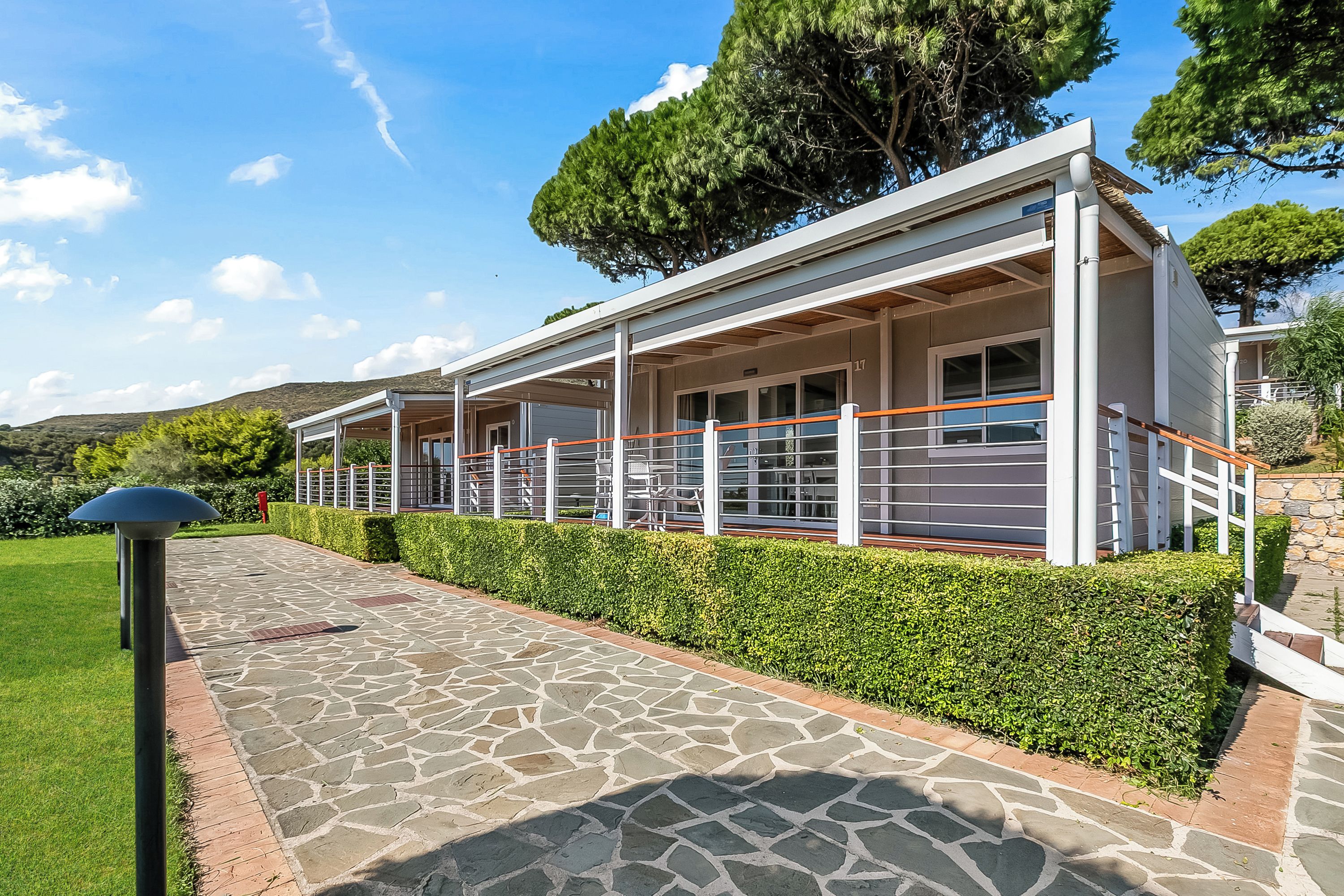 Un edificio moderno con un'area esterna coperta, un vialetto in pietra e siepi curate.