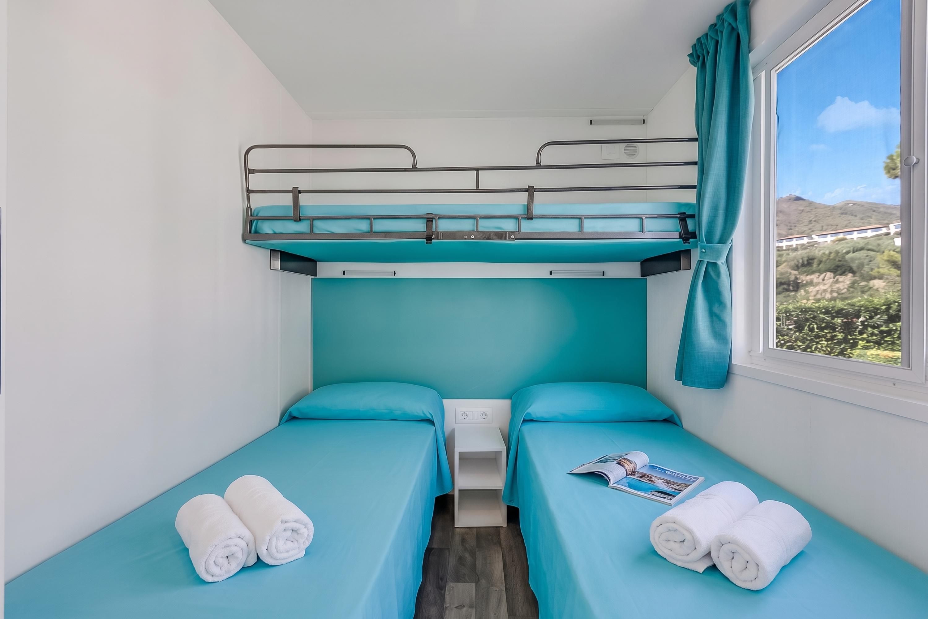 Ein kleines Zimmer mit Etagenbetten, einem kleinen Nachttisch und einem Fenster mit Landschaftsblick.
