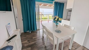 Eine moderne Küche mit weißen Schränken, ein Essbereich mit weißem Tisch und Stühlen sowie Meerblick durch eine Glastür.