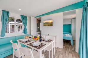 A modern, well-lit room with teal accents, a dining area with a table set for two, and a bed with teal curtains. - Sea View - 40 Parallelo - Premium 14, Marina di Camerota, Italy (Marina di Camerota)