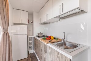 Cocina compacta con armarios blancos, estufa integrada, un lavabo y una encimera de madera con verduras.