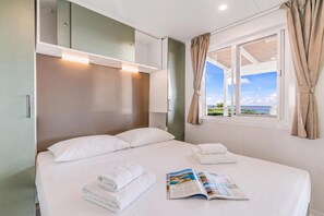 Habitación de hotel con cama, ventana con cortinas, una revista sobre la cama y vista al mar.