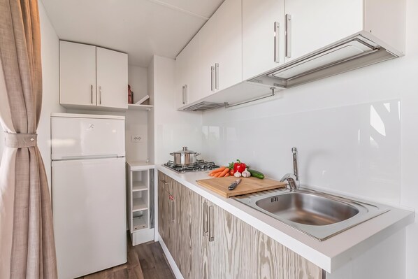 Una cocina compacta con armarios blancos, estufa integrada y pileta de acero inoxidable.