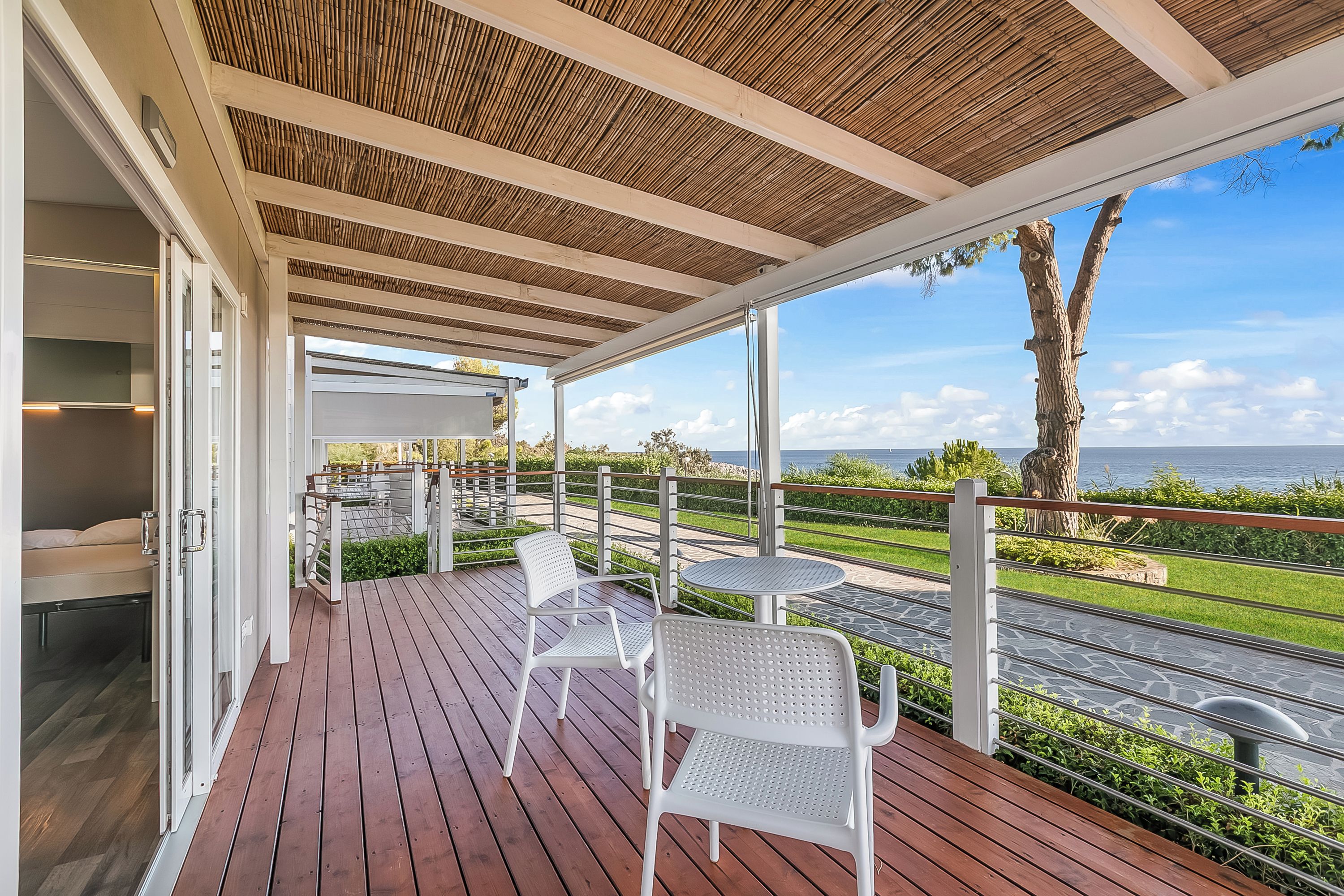 Un espacio al aire libre cubierto con una terraza de madera, sillas blancas y vista al mar.