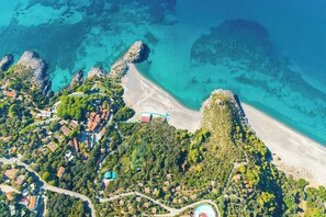 Eine Luftaufnahme einer Küstenregion mit Strand, Wohnhäusern und einem Schwimmbad.