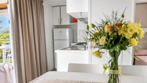 A kitchen with a refrigerator, stove, and cabinets. There is a dining table with a vase of flowers. - Sea View - 40 Parallelo - Superior 12, Marina di Camerota, Italy (Marina di Camerota)