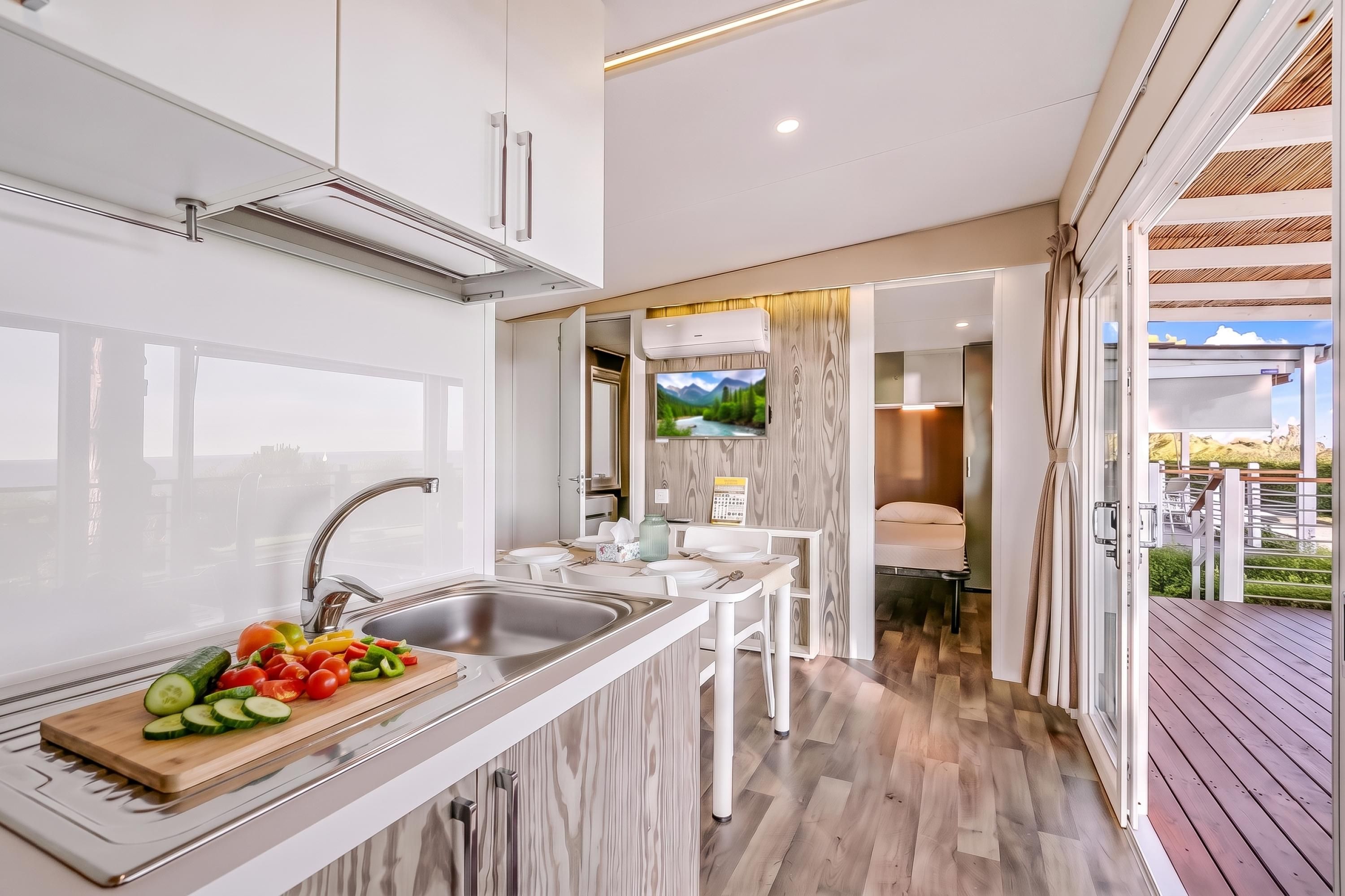 A modern kitchen with a built-in stove, a sink, and a wooden cutting board with vegetables.