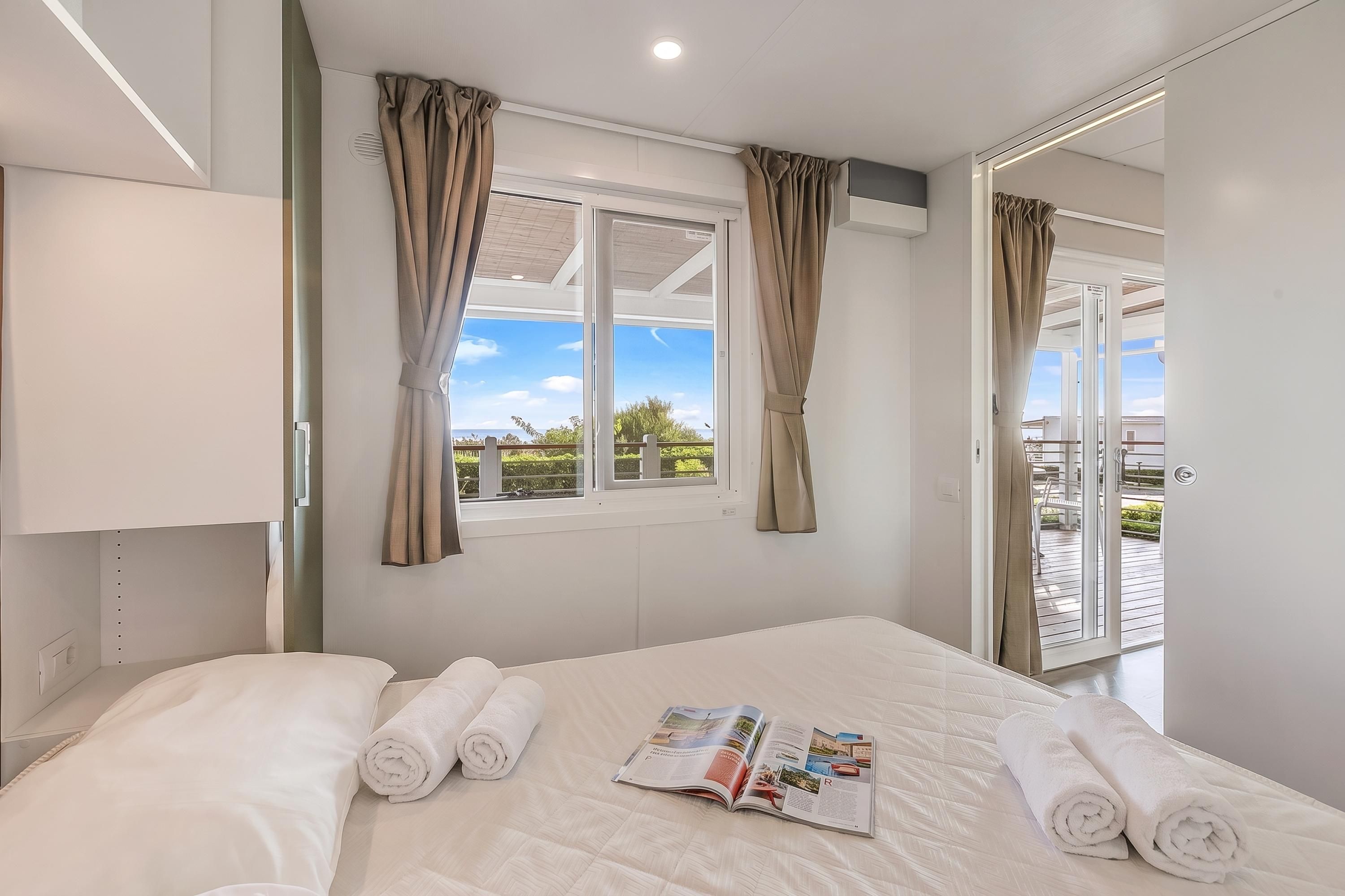 A hotel room with a bed, a window with curtains, a door, and a view of the outdoors.