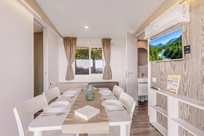 Un coin repas avec une table dressée pour six personnes, une fenêtre avec des rideaux et un téléviseur fixé au mur.