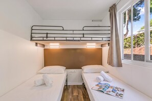 Une chambre avec un lit superposé comprenant deux lits simples, une fenêtre avec des rideaux et un magazine posé sur le lit.