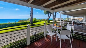 Un espace extérieur abrité, avec vue sur la mer, doté d’un plancher en bois et de chaises blanches.