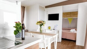 Une chambre d’hôtel moderne dotée d’une kitchenette, d’un coin repas avec une table et des chaises, d’un lit recouvert d’une courtepointe rose et d’un téléviseur fixé au mur.