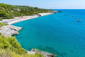 Une plage côtière aux eaux turquoise et limpides, bordée de falaises rocheuses et parsemée de quelques bateaux.