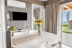 A modern room with a flat-screen TV mounted on the wall, a dining table with chairs, a vase with flowers, and a view of the outdoors through a door. - Sea View - 40 Parallelo - Superior 10, Marina di Camerota, Italy (Marina di Camerota)