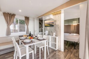 Une pièce moderne et bien éclairée, avec une table à manger dressée pour deux personnes, un lit doté d’un matelas blanc et une vue sur un paysage pittoresque.