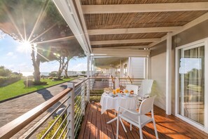 Un balcón con cubierta de madera, muebles de exterior blancos y una mesa preparada para el desayuno.