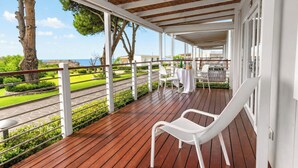 Et overdækket udendørs område med trægulv, hvide stole og et bord dækket til spisning.