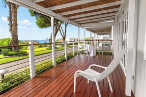 Uma área externa coberta com piso de madeira, cadeiras brancas e uma mesa posta para refeições.