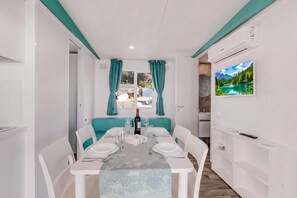 A compact, modern room with a dining table set for two, a sofa, and a TV mounted on the wall.