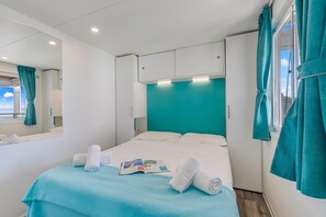 A hotel room with a bed, a window with curtains, a mirror, and a ceiling light.