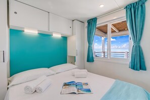 Ein Schlafzimmer mit Bett, einem Fenster mit Vorhängen und Meerblick.