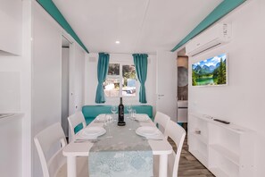 Uma área de refeições com uma mesa posta para quatro pessoas, uma garrafa de vinho e vista para uma paisagem montanhosa pela janela.