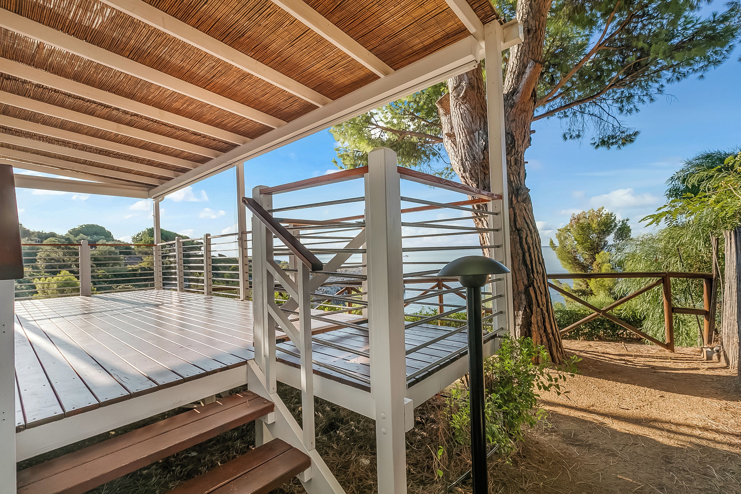 Un espace extérieur abrité, doté d’une terrasse en bois, d’une rambarde en métal et offrant une vue sur le paysage environnant.