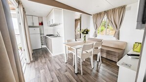 A compact kitchen with white cabinets, a dining area with a table and chairs, and a living area with a sofa and a TV.