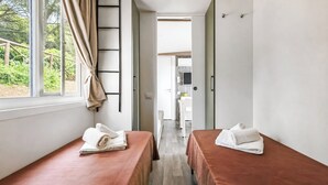 A room with two beds, a window with curtains, a door, and a view of a garden.