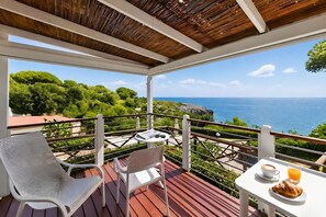 A balcony with a wooden ceiling, white chairs, a table with a croissant and juice, and a view of the sea and greenery. - Sea View - 40 Parallelo - Superior 8, Marina di Camerota, Italy (Marina di Camerota)