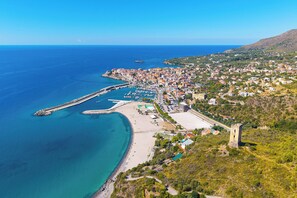 An aerial view of a coastal town with a marina, beach, and historic tower. - Sea View - 40 Parallelo - Superior 8, Marina di Camerota, Italy (Marina di Camerota)
