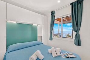 A bedroom with a bed, a window with curtains, and a view of the sea. - Sea View - 40 Parallelo - Deluxe 7, Marina di Camerota, Italy (Marina di Camerota)