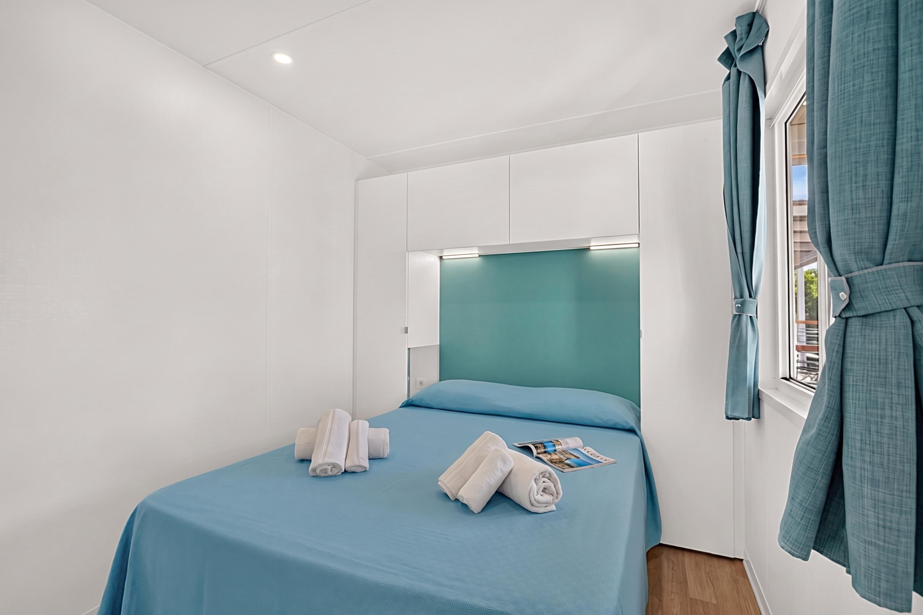 A hotel room with a bed, a window with curtains, and a headboard with built-in lighting.