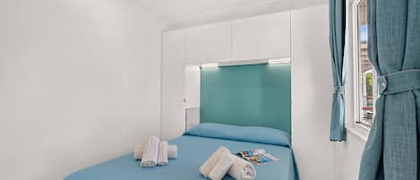 A hotel room with a bed, a window with curtains, and a headboard with built-in lighting.