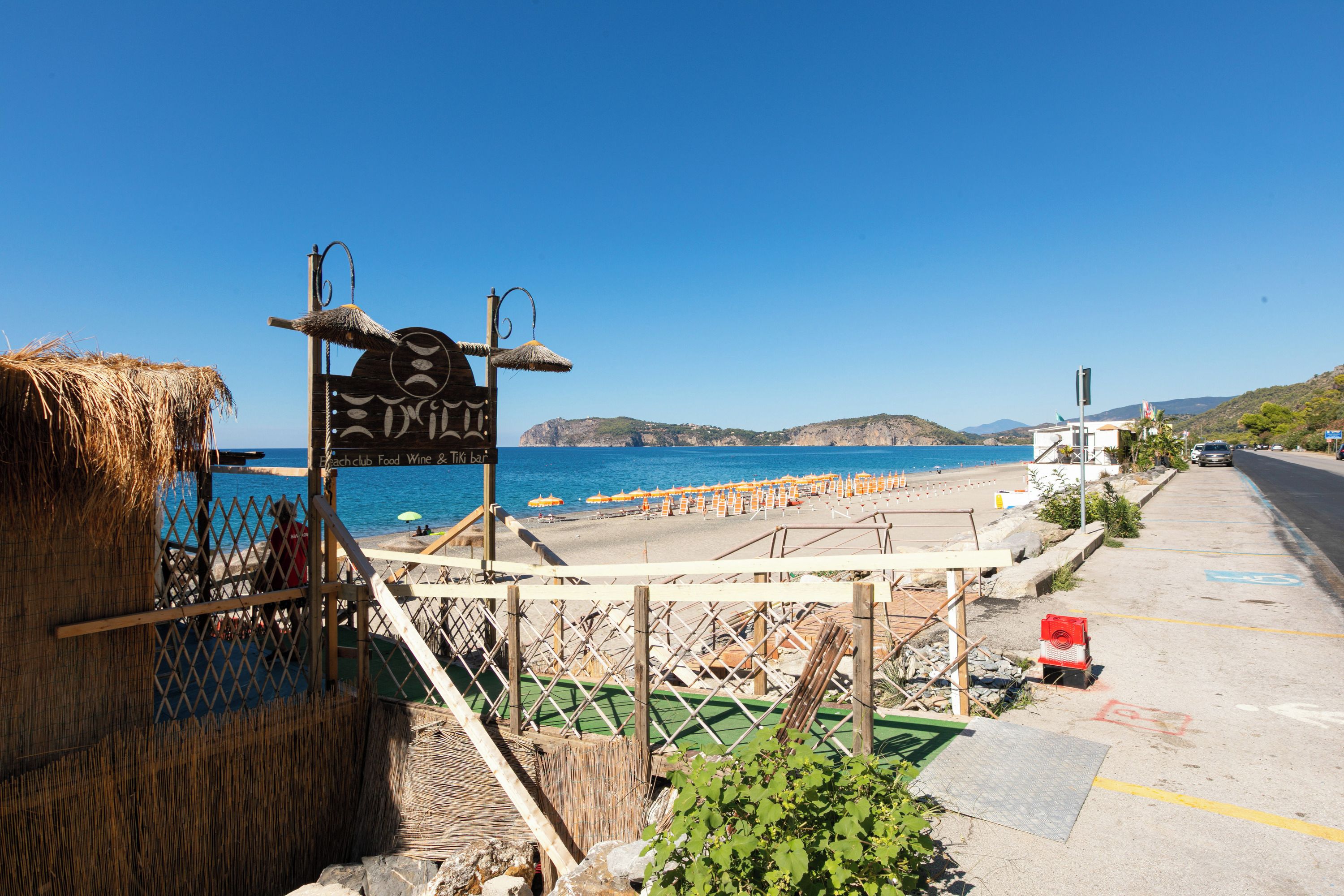 Uitzicht op het strand met een bordje voor een strandclub, eten, wijn en een tiki bar.